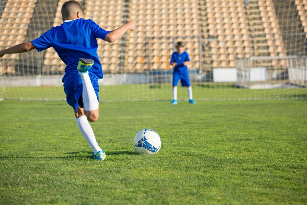 Two boys in blue uniforms practice soccer on a sunny field, focusing on the ball.